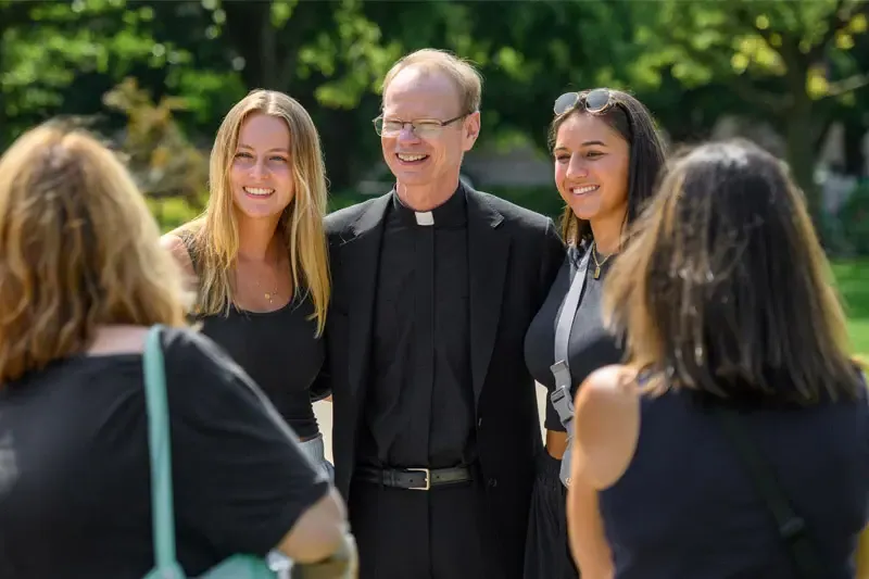 A photo of Fr. Dowd standing in a crowd of female students